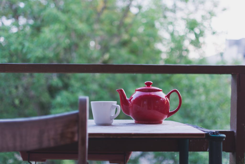red teapot and white teacup on small table with chair on outside deck in trees