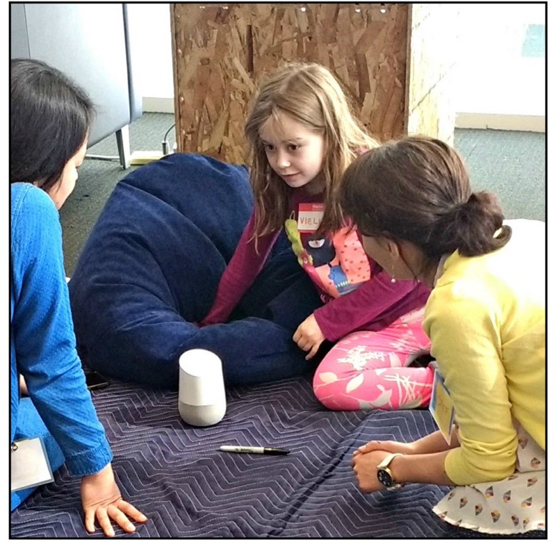 3 children kneeling on floor speaking to Google Home device