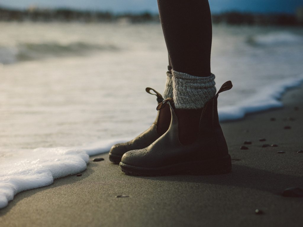 Young person wearing boots standing at ocean edge on sand