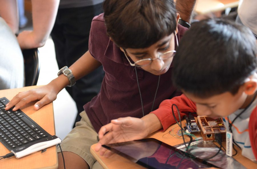 one older boy with laptop working with a younger boy who has a tablet computer in his hands