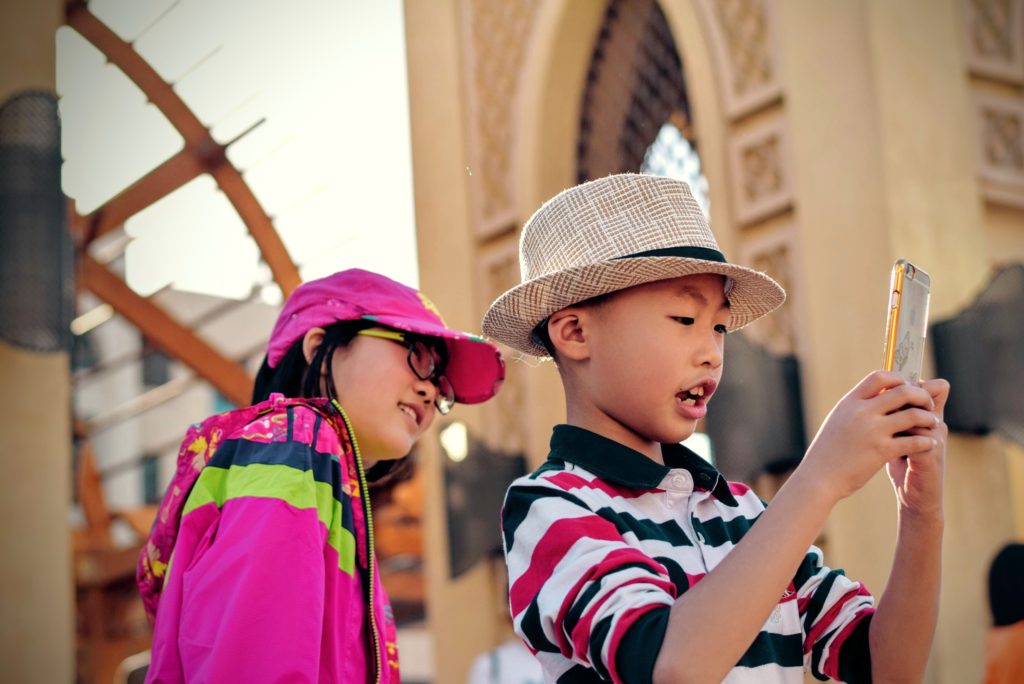 Young boy holding and looking at something on an iPhone while young girl looks over his shoulder at phone too