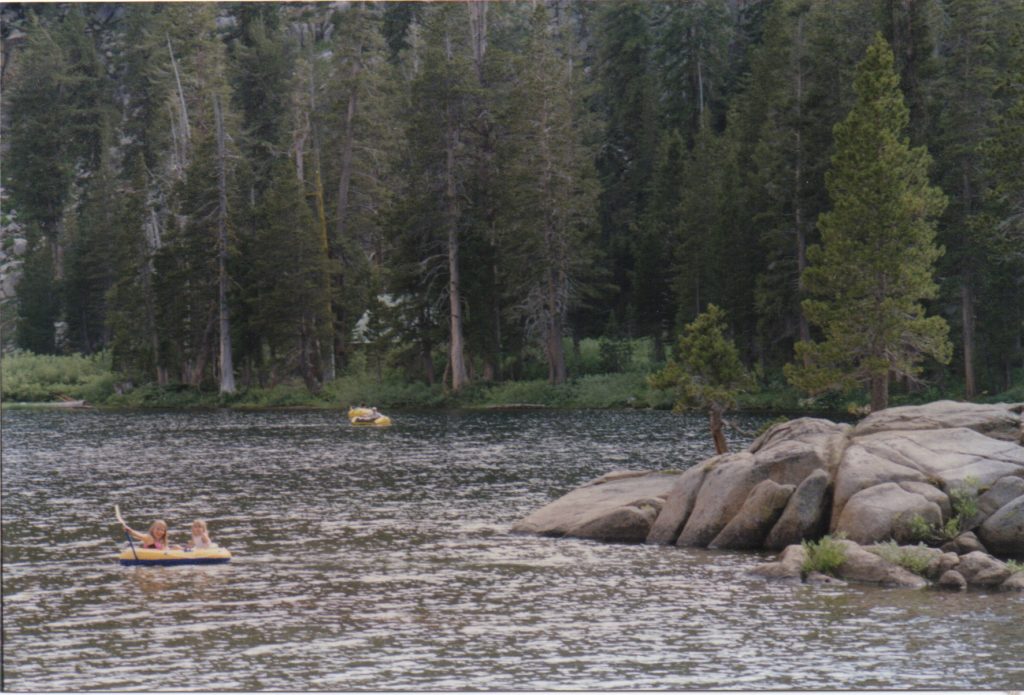 Lake with 2 kids in a small yellow rubber boat and with tall pines in background