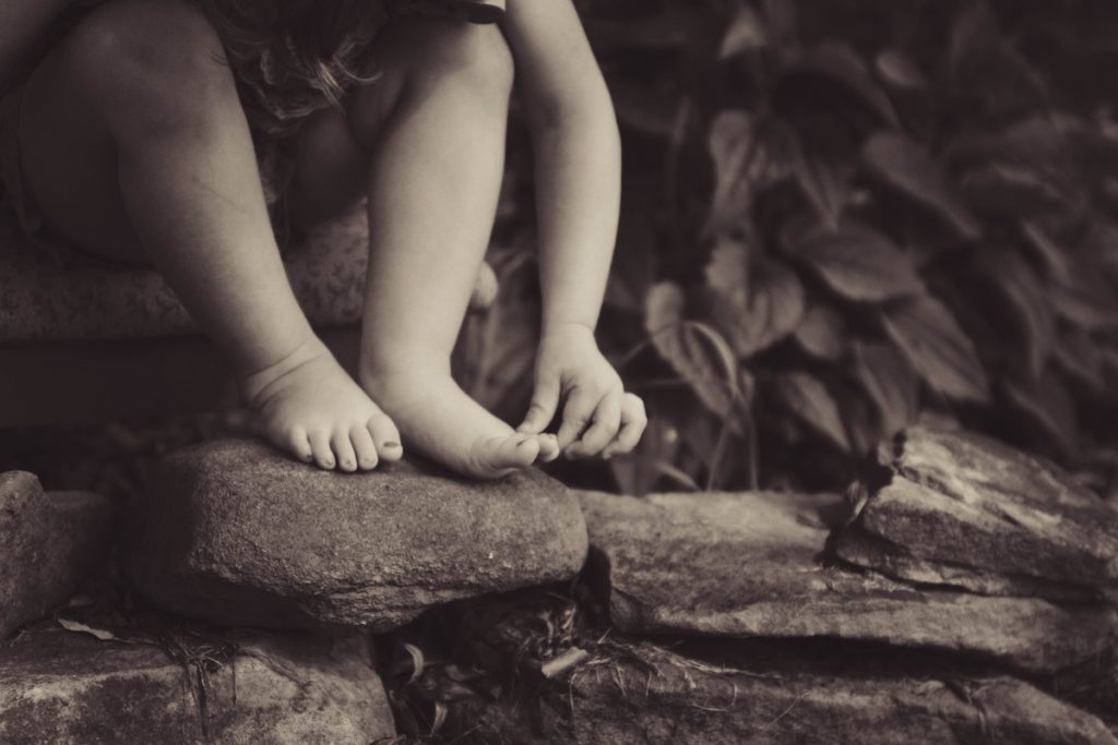 black and white photo of legs feet and arm of small child on rocks
