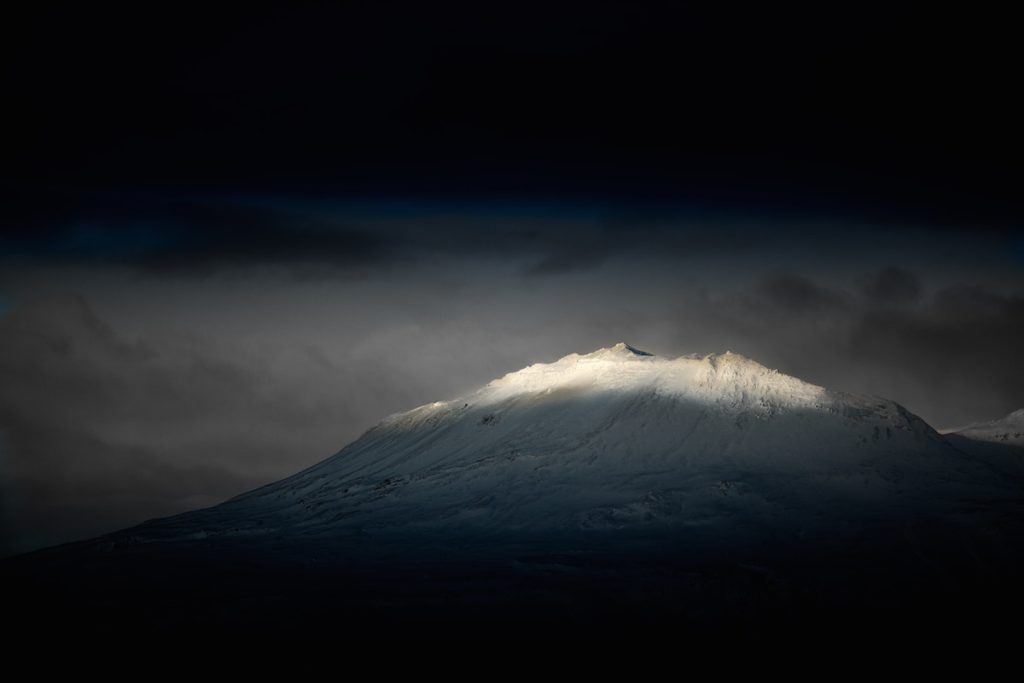 mountain with summit illuminated by sun through clouds