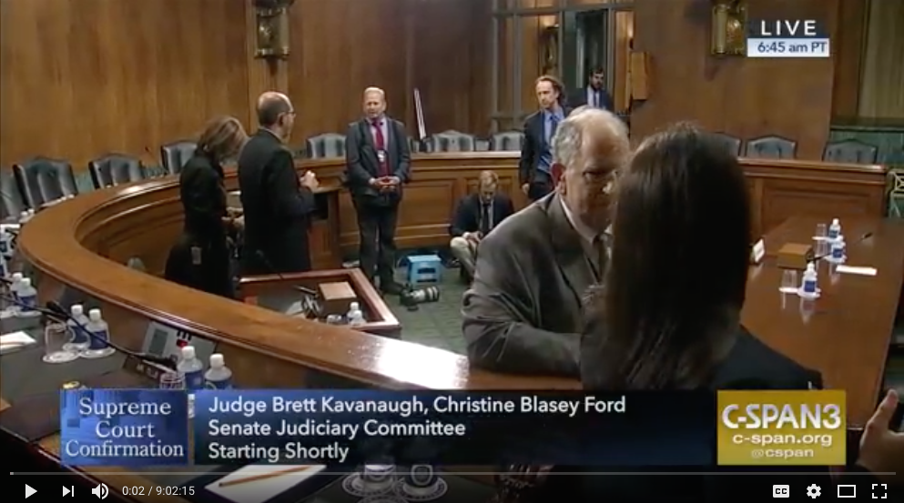 screenshot of video showing several men standing and talking before Senate hearing of Ford and Kavanaugh
