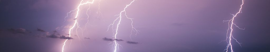 lightning bolts in purple night sky with a few clouds